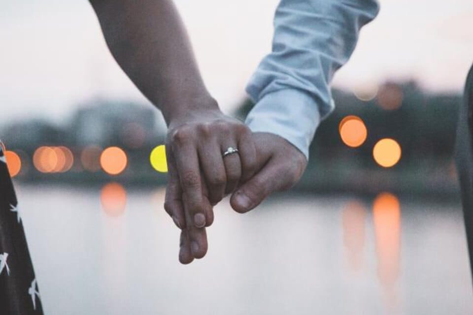 A couple holding hands at sunset after getting engaged
